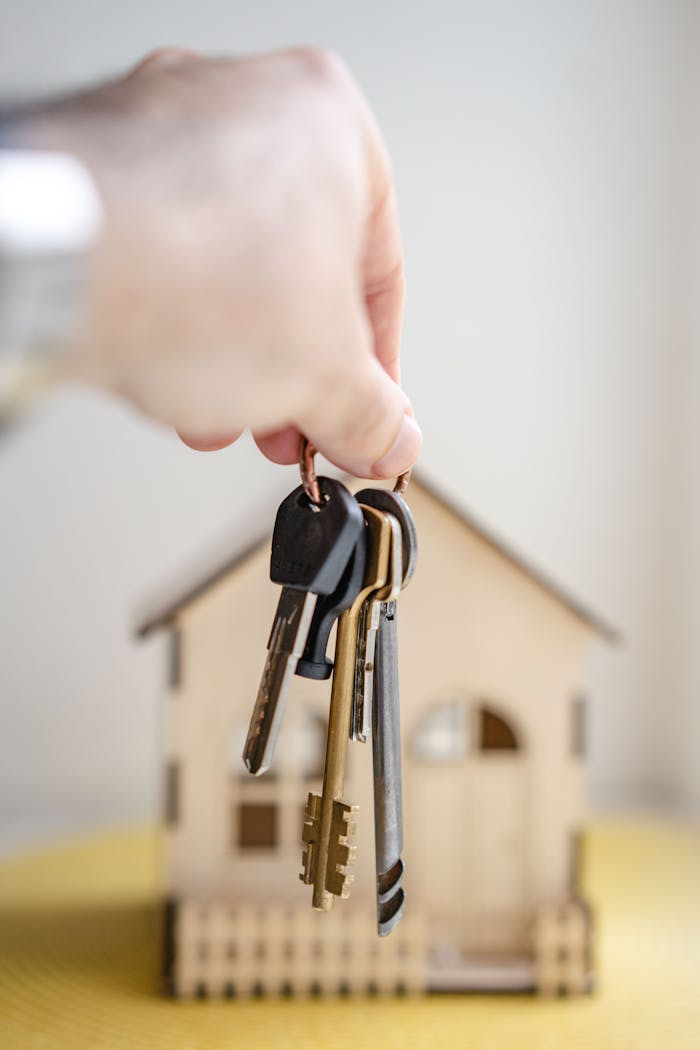 services-02 Crop faceless real estate agent with keys from new house bought with mortgage against wooden model of building